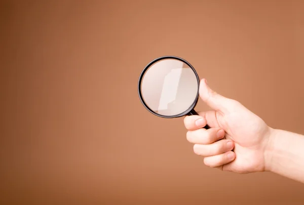 Hand holding magnifying glass on the beige background — Stock Photo, Image