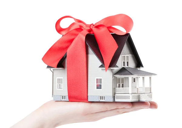 Mão segurando modelo de casa com arco vermelho — Fotografia de Stock