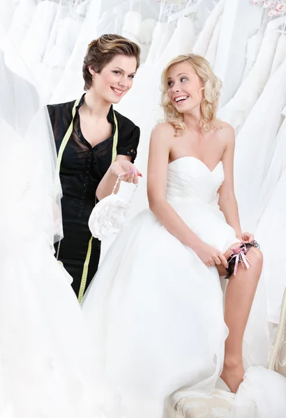Verkäuferin gibt Rat, während zukünftige Braut das Strumpfband anlegt — Stockfoto
