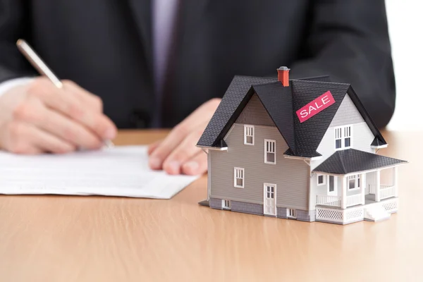 Businessman signs contract behind household architectural model — Stock Photo, Image