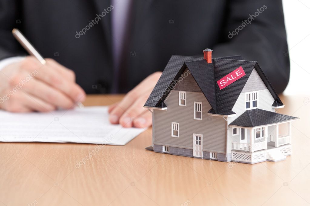 Businessman signs contract behind household architectural model