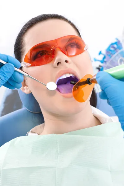 Dentist uses photopolymer lamp and dental mirror to treat teeth — Stock Photo, Image