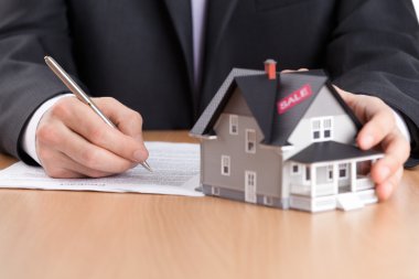 Businessman signs contract behind house architectural model clipart