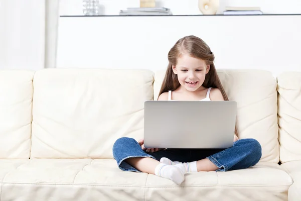 stock image Little child sits on the sofa with laptop