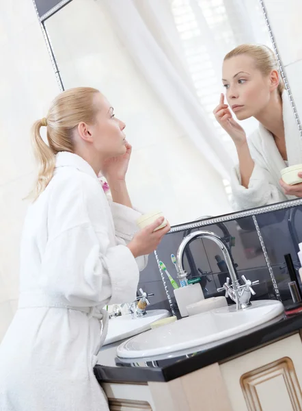 Jolie femme crèmes son visage dans salle de bain — Photo