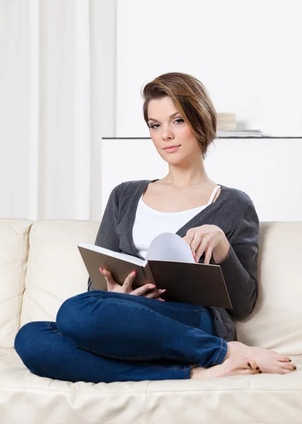 Hübsche Frau liest das Buch sitzend auf dem Sofa — Stockfoto