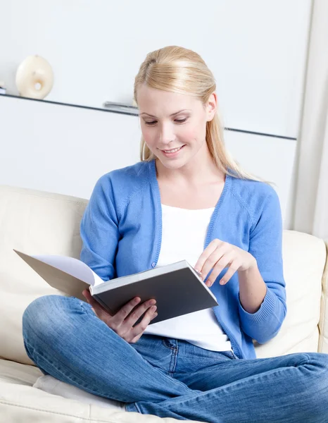Beautiful woman reads the book lying on the sofa — Stock Photo, Image