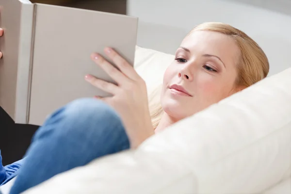 Ung tjej läser boken liggande på soffan — Stockfoto