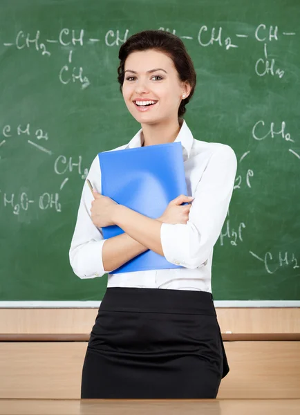 Laughing teacher at the blackboard hands a folder — Stock Photo, Image
