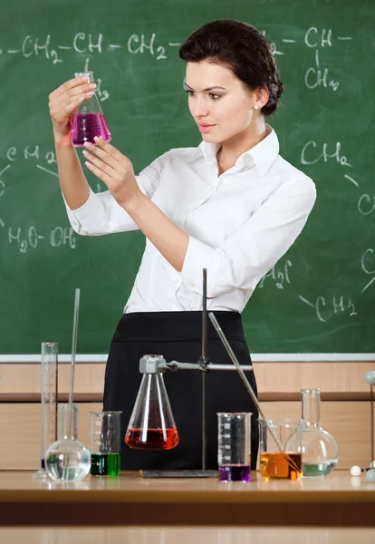 Smiley chemistry teacher examines conical flask — Stock Photo, Image
