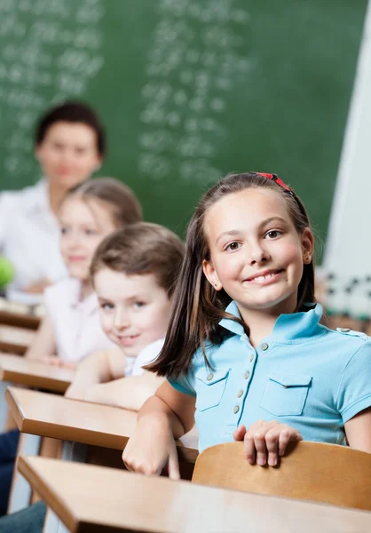 Smiley schoolgirl sits at the desk — Stock Photo, Image