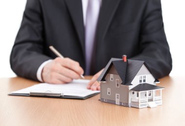 Businessman signs contract behind home architectural model clipart