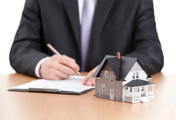 Businessman signs contract behind home architectural model — Stock Photo, Image