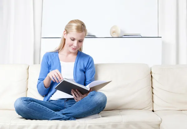 Женщина читает книгу, лежащую на диване — стоковое фото
