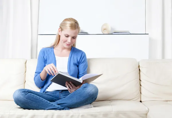 stock image Woman reads the book lying on the sofa