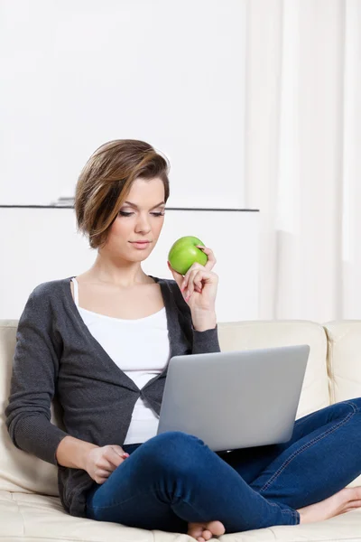 Woman eats a green apple surfing on the internet — Stock Photo, Image