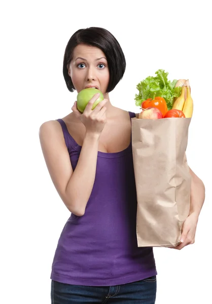 Αρκετά νεαρή γυναίκα με το πακέτο που είναι γεμάτο από υγιεινά τρόφιμα τρώει ένα μήλο — Φωτογραφία Αρχείου