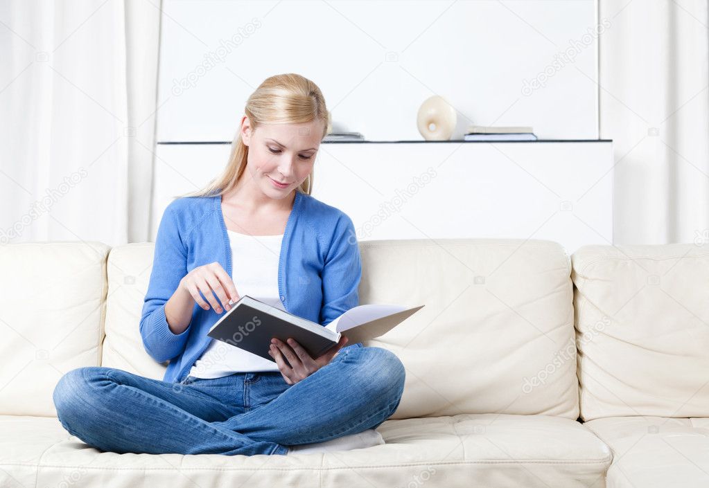 Woman reads the book lying on the sofa