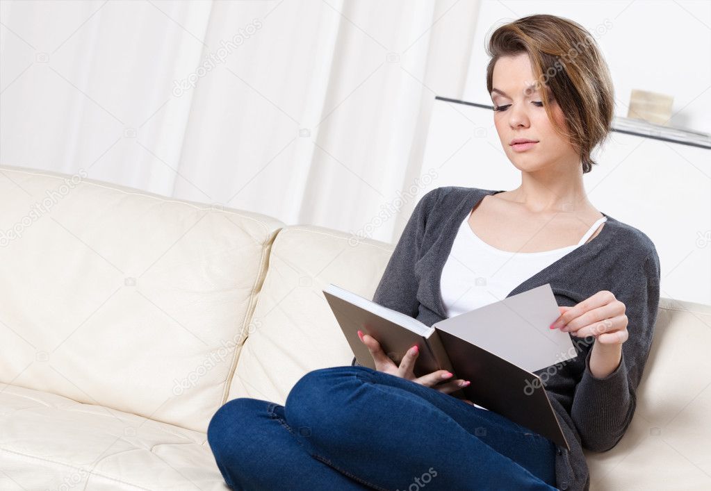 Young girl reads the book sitting on the sofa