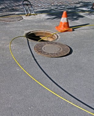 Open manhole with yellow optic cables, telecommunication details. clipart