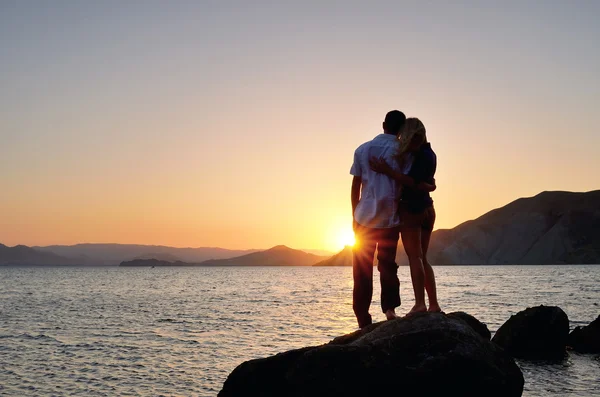 Чоловік і жінка стоять в обіймах і спостерігають за заходом сонця — стокове фото