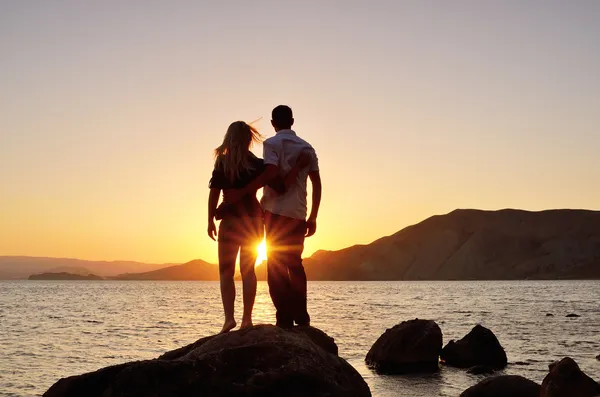 Jovem casal observando o sol junto ao mar — Fotografia de Stock