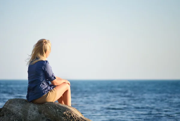 Chica está sentada en una roca y mirando al mar —  Fotos de Stock