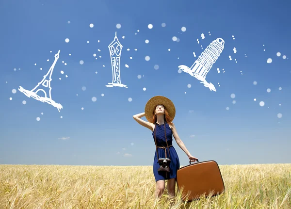 Рыжая девушка с чемоданом на пшеничном поле . — стоковое фото