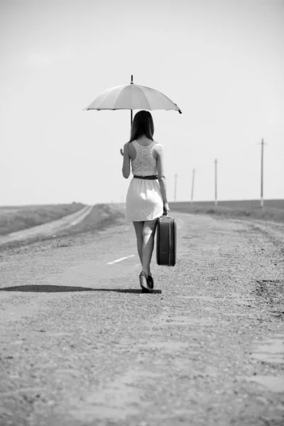 Eenzaam meisje met koffer en umrella op land road. — Stockfoto