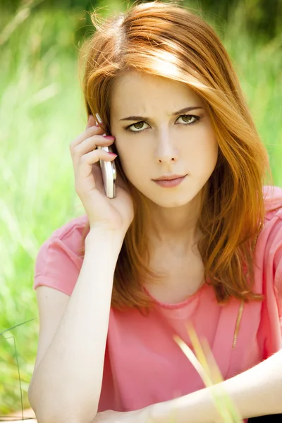 Злая рыжая девушка с мобильным телефоном в парке . — стоковое фото