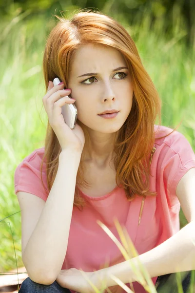 Angry redhead girl with mobile phone at the park. — Stock Photo, Image