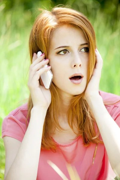 Boos roodharige meisje met mobiele telefoon in het park. — Stockfoto
