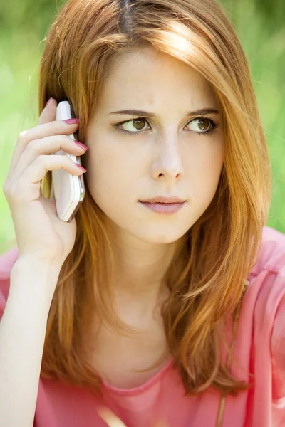 Boos roodharige meisje met mobiele telefoon in het park. — Stockfoto