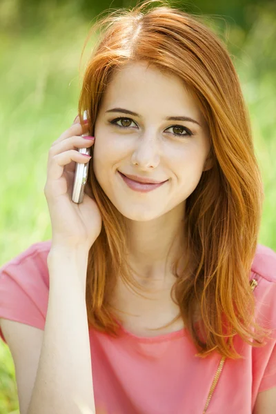 Roodharige meisje met mobiele telefoon in het park. — Stockfoto