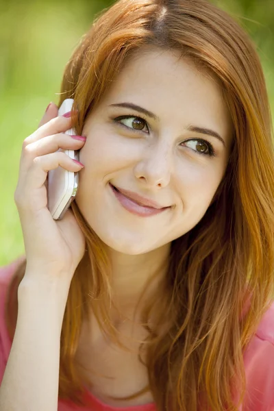Roodharige meisje met mobiele telefoon in het park. — Stockfoto
