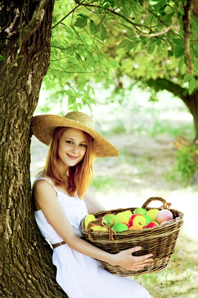 Schöne rothaarige Mädchen mit Früchten im Korb im Garten. — Stockfoto