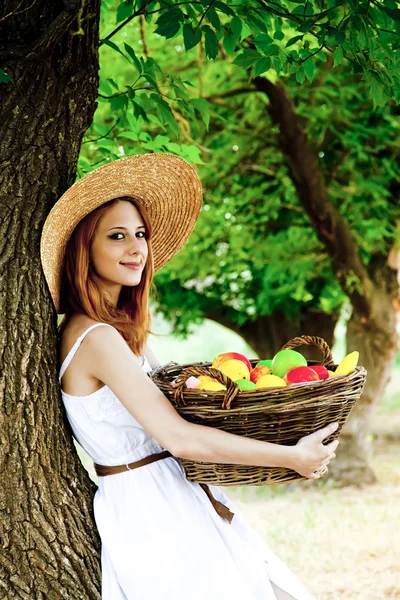 Όμορφη κοκκινομάλλα κοπέλα με τα φρούτα στο καλάθι σε κήπο. — Φωτογραφία Αρχείου