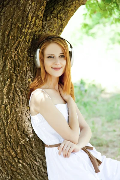 Hermosa pelirroja con auriculares en el jardín . — Foto de Stock