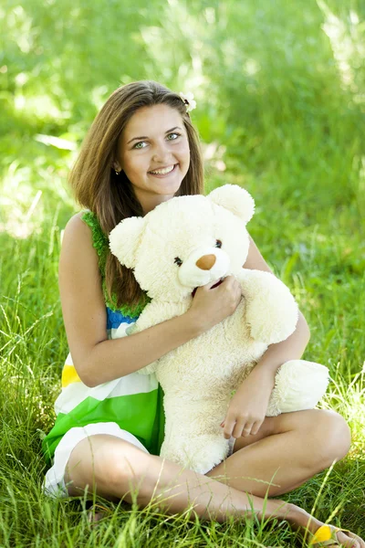 Beautiful teen girl with Teddy bear in the park at green grass. — Stock Photo, Image