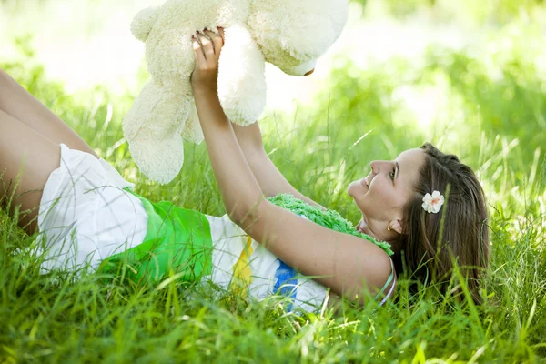 美丽的年轻女孩与玩具熊在公园在绿草. — 图库照片
