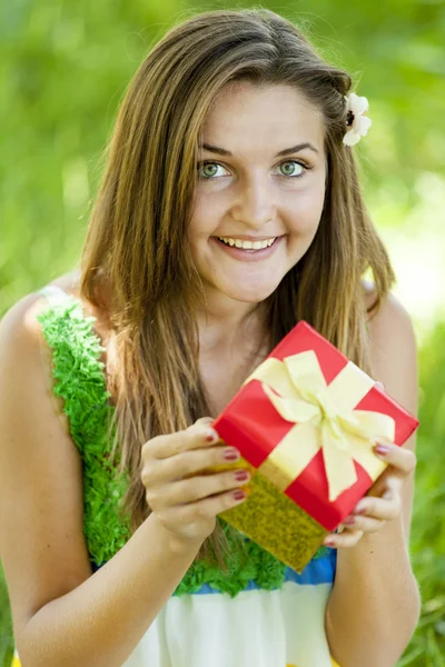 Mooie tiener meisje met cadeau in het park op groen gras. — Stockfoto