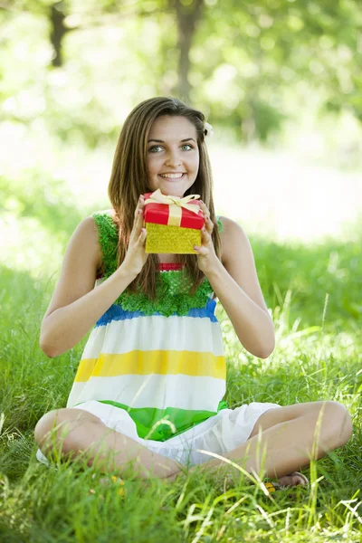 Красивая девушка-подросток с подарком в парке на зеленой траве . — стоковое фото