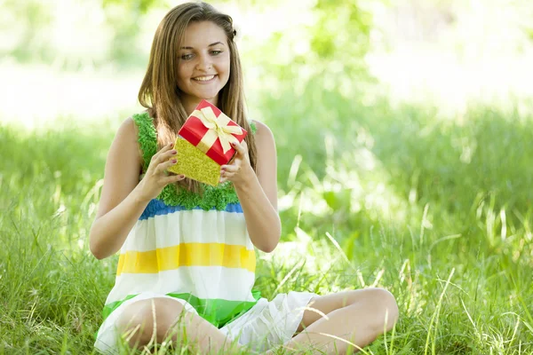 Krásná dospívající dívka s darem v parku na zelené trávě. — Stock fotografie