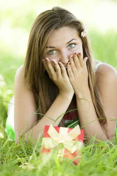Verrast mooie tiener meisje met cadeau in het park op groene gra — Stockfoto