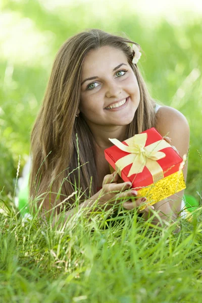 Όμορφο κορίτσι, με δώρο στο πάρκο στο πράσινο γρασίδι. — Φωτογραφία Αρχείου