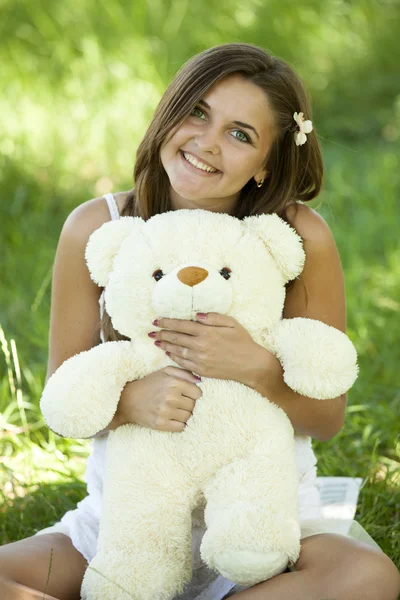 Mooie tiener meisje met teddy beer in het park op groen gras. — Stockfoto