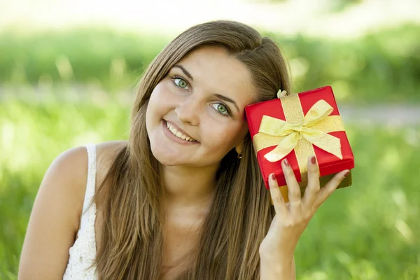 Mooie tiener meisje met cadeau in het park op groen gras. — Stockfoto