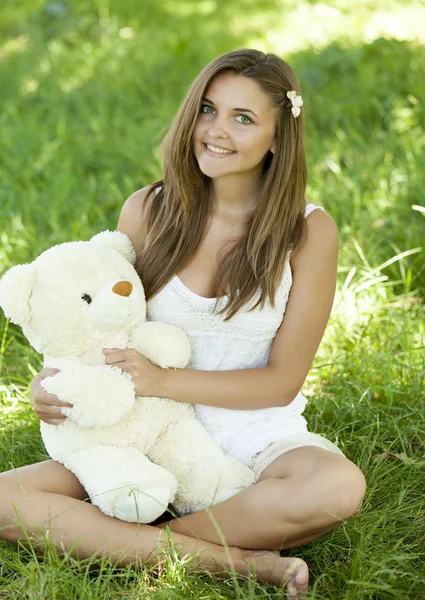 Красива підлітків дівчина з ведмедиком в парку, на зеленій траві. — стокове фото