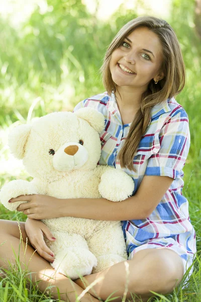 Mooie tiener meisje met teddy beer in het park op groen gras. — Stockfoto