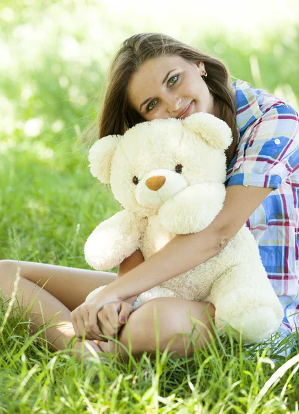 Красивая девушка-подросток с плюшевым мишкой в парке на зеленой траве . — стоковое фото